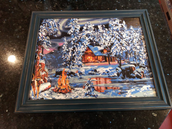 Aurora Bliss paint by numbers completed by Joan H: a lit cabin in snowy pines beside a campfire under the northern lights