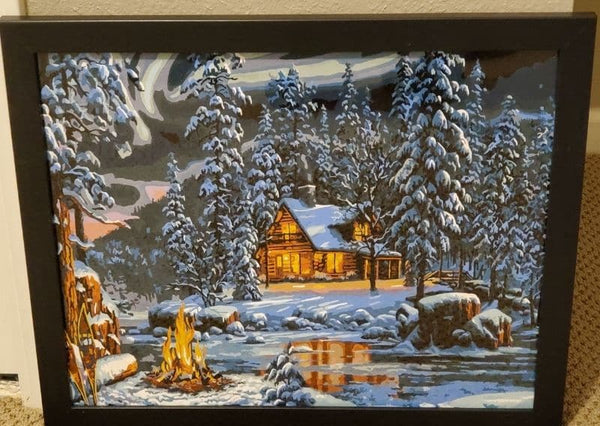 Aurora Bliss paint by numbers completed by Janine O: a lit cabin in snowy pines beside a campfire under the northern lights